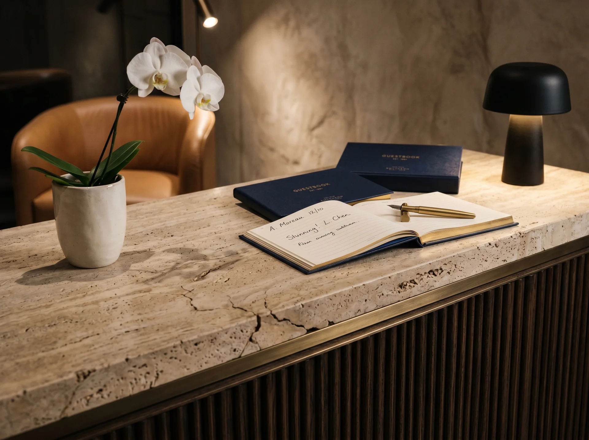 Detalle de mostrador de check-in en travertino, latón cepillado y madera con iluminación dirigida y orquídea