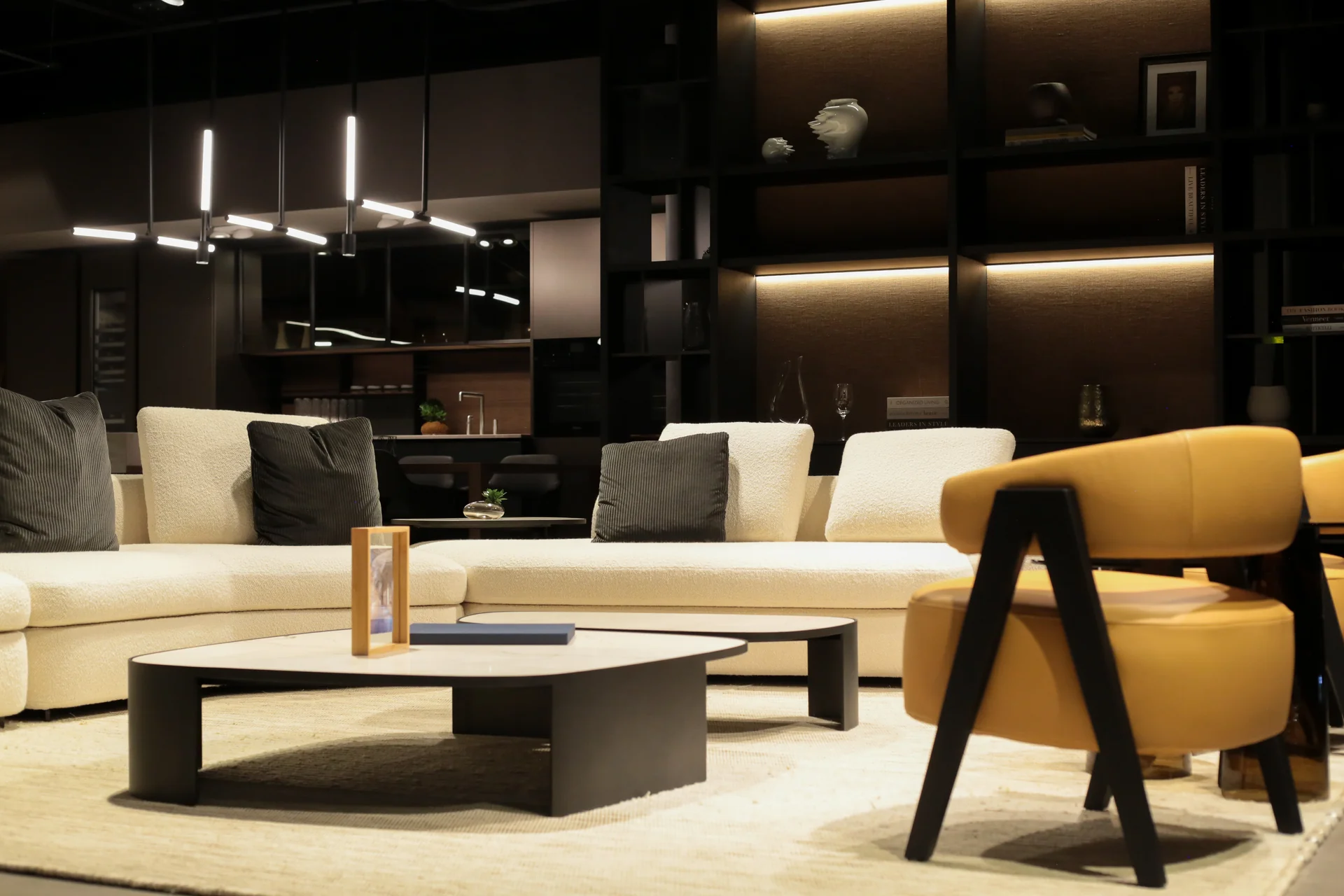 Sala Poliform con sofá boucle curvo blanco, sillón mostaza en cuero y librería de pared retroiluminada · showroom Productos Arquitectónicos en Bogotá