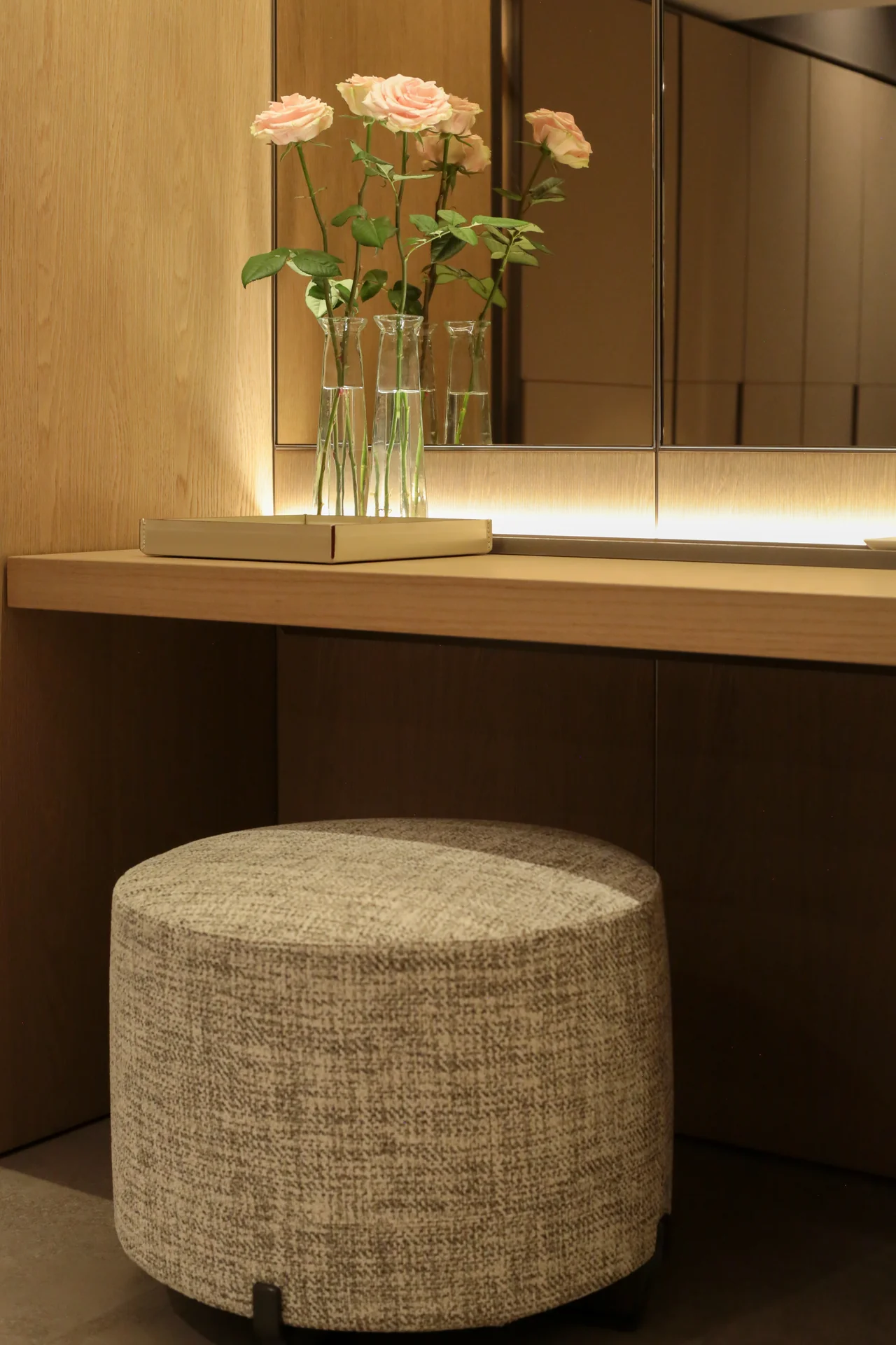 Tocador del sistema de vestidores Poliform con rosas en jarrones de vidrio y banco en textil natural texturizado · showroom Productos Arquitectónicos en Bogotá