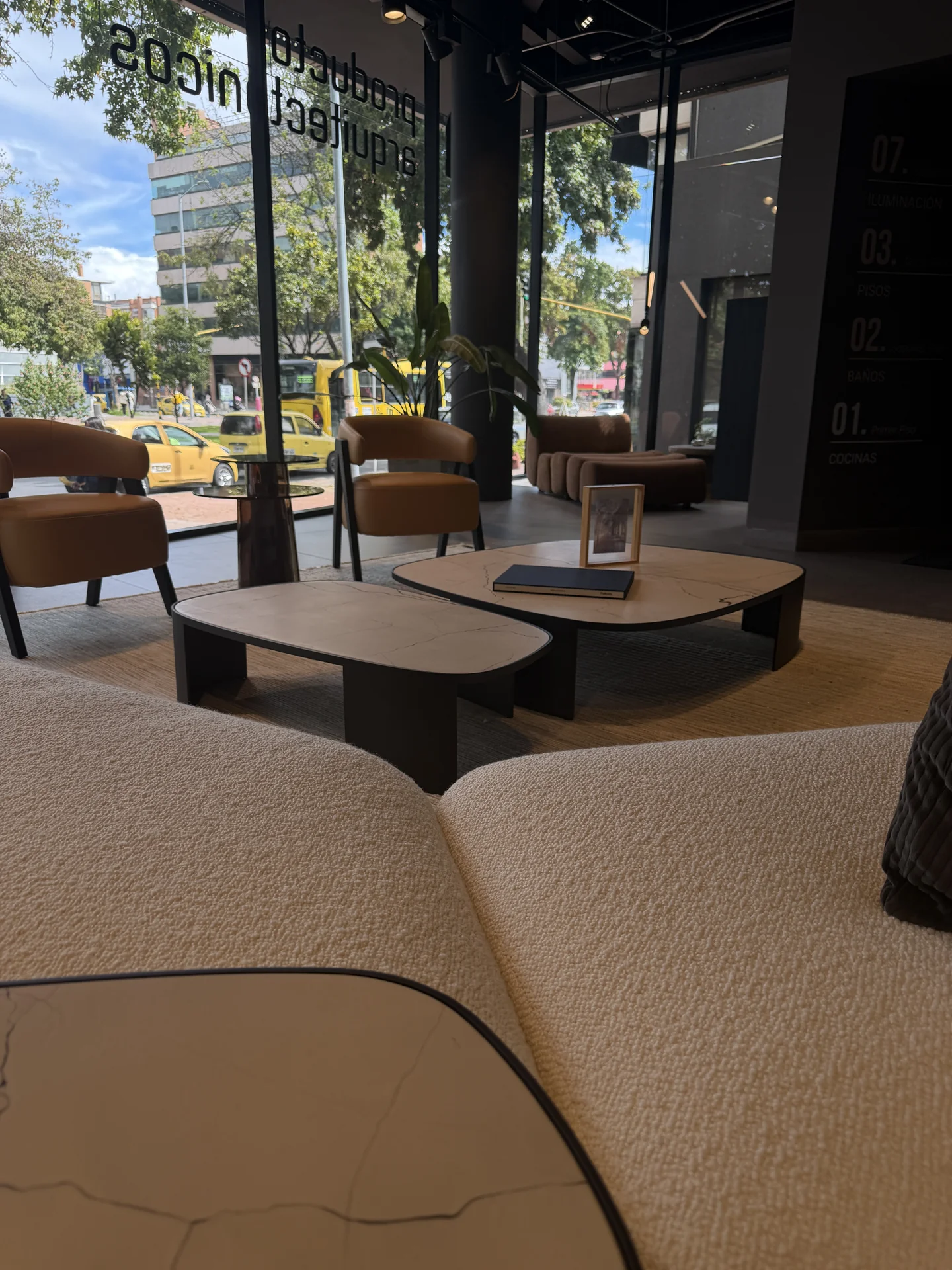 Mesas en mármol y sillón en cuero mostaza Poliform con la fachada del showroom de Productos Arquitectónicos al fondo · Bogotá